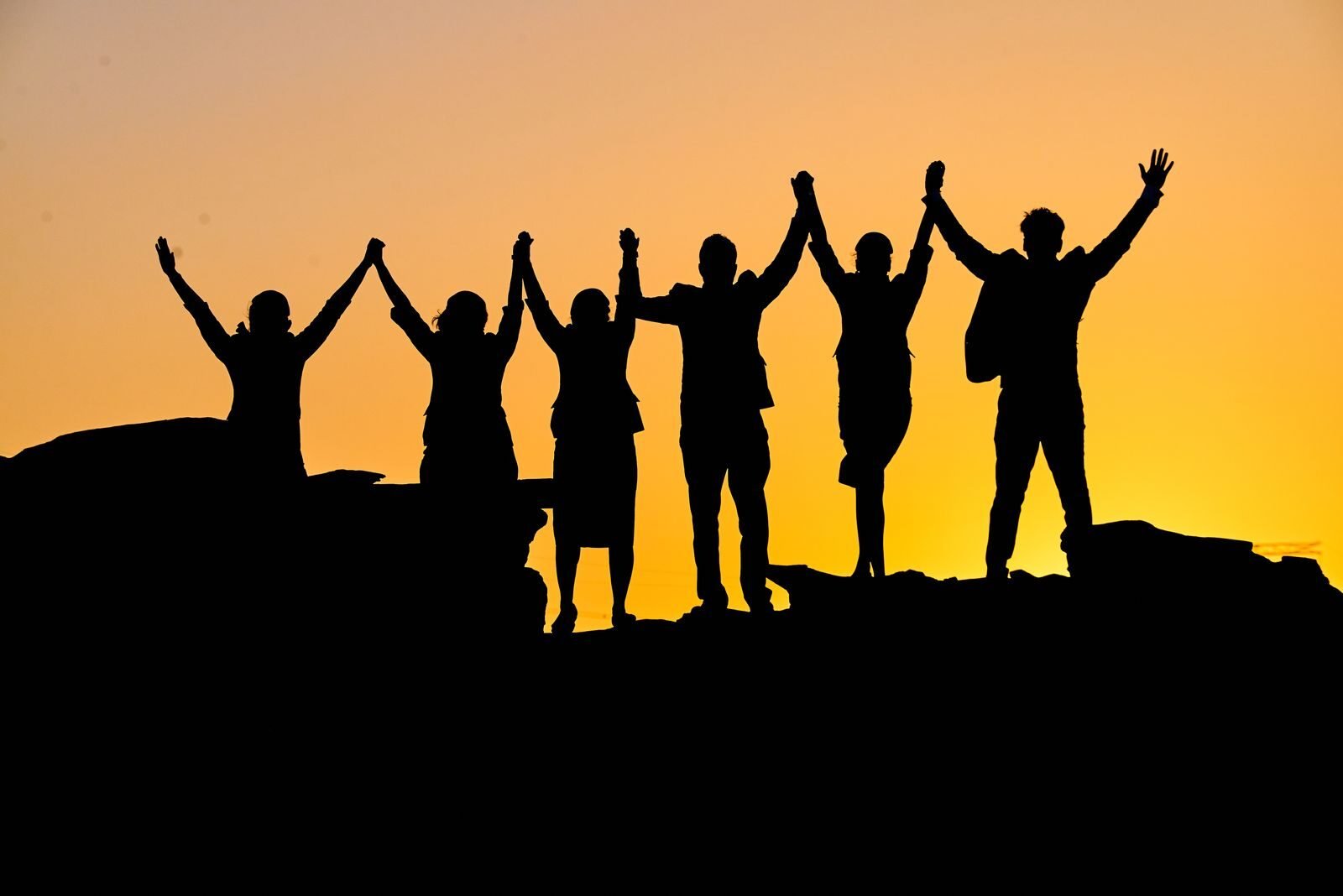 Photo by Wilfred Panakkal A group of silhouetted people holding hands triumphantly at sunset.